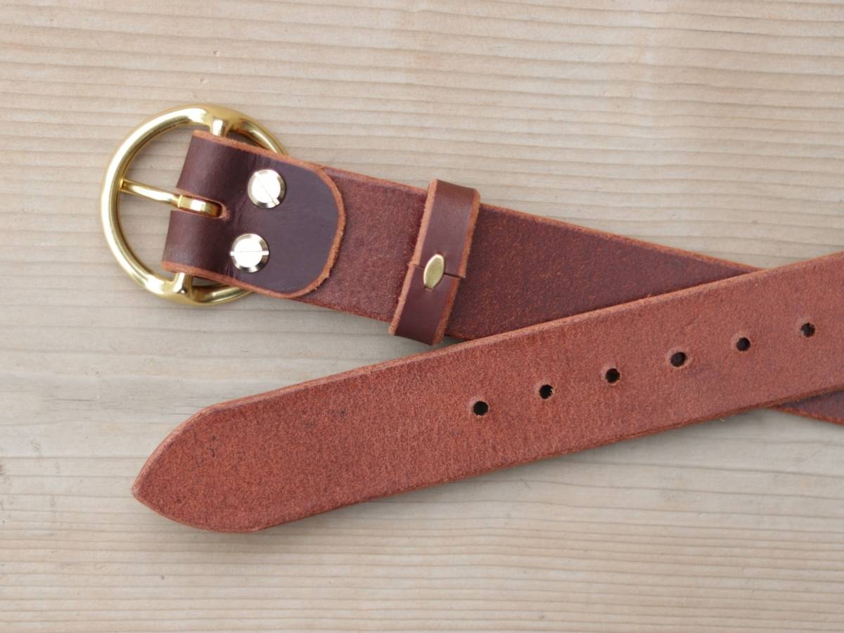 A ladies brown leather belt with a gold-tone metal buckle and silver-tone rivets, laid flat on a light wood grain background.