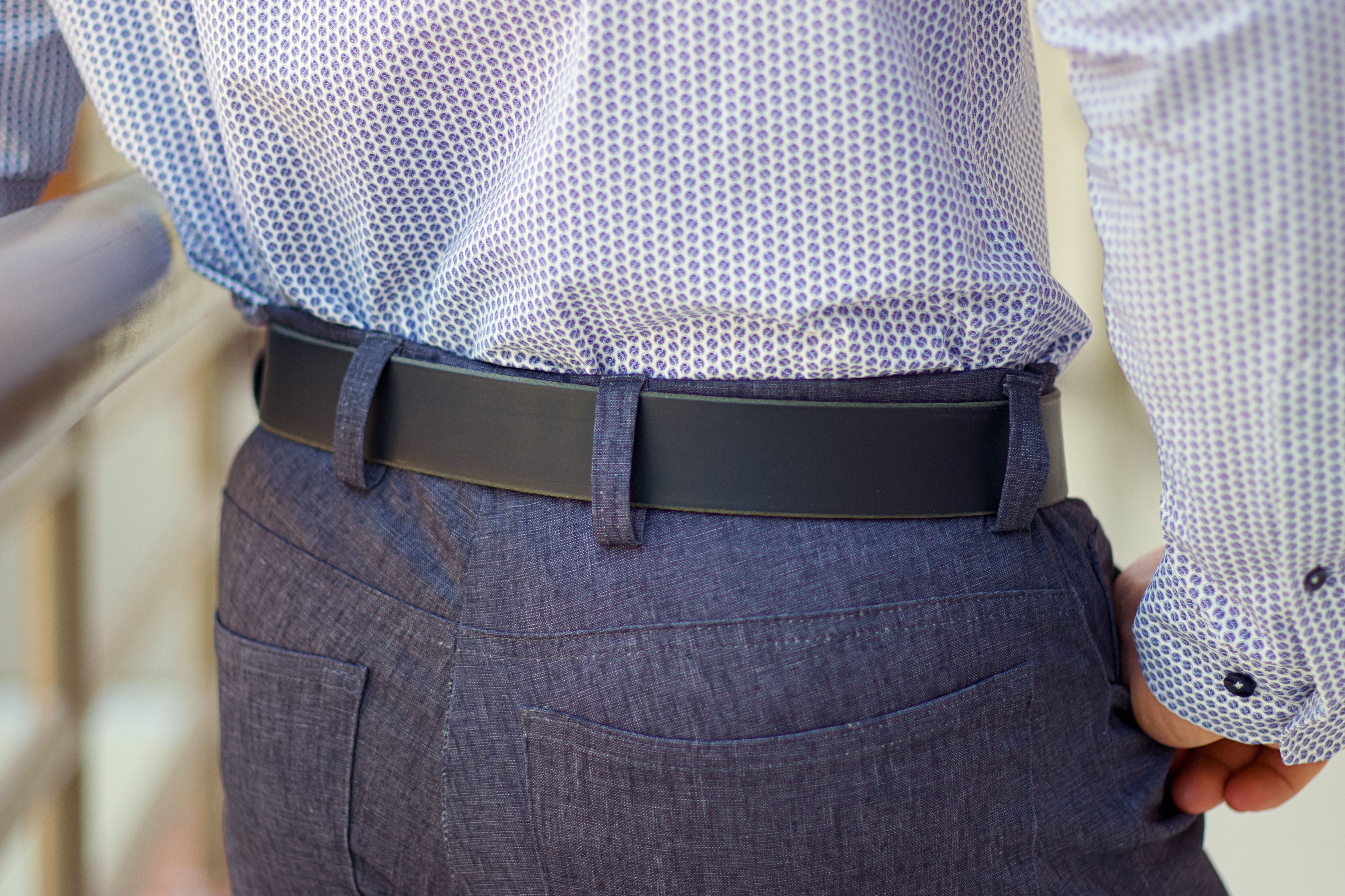 Person wearing a patterned shirt, dark belt, and gray pants.