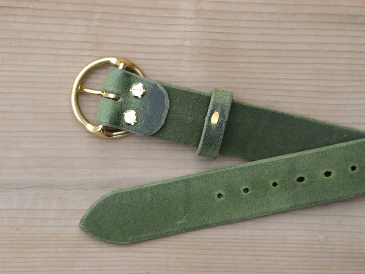 An olive green suede belt with a gold-tone metal buckle and hardware, laid out on a light wood grain background.