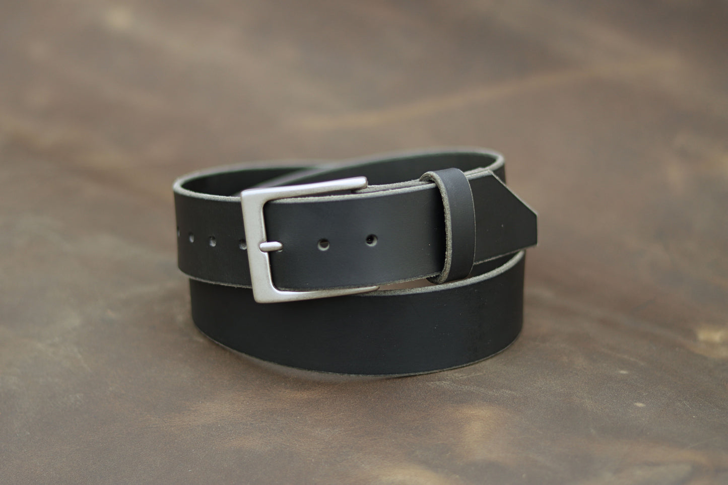 Black leather belt with silver buckle on a brown surface