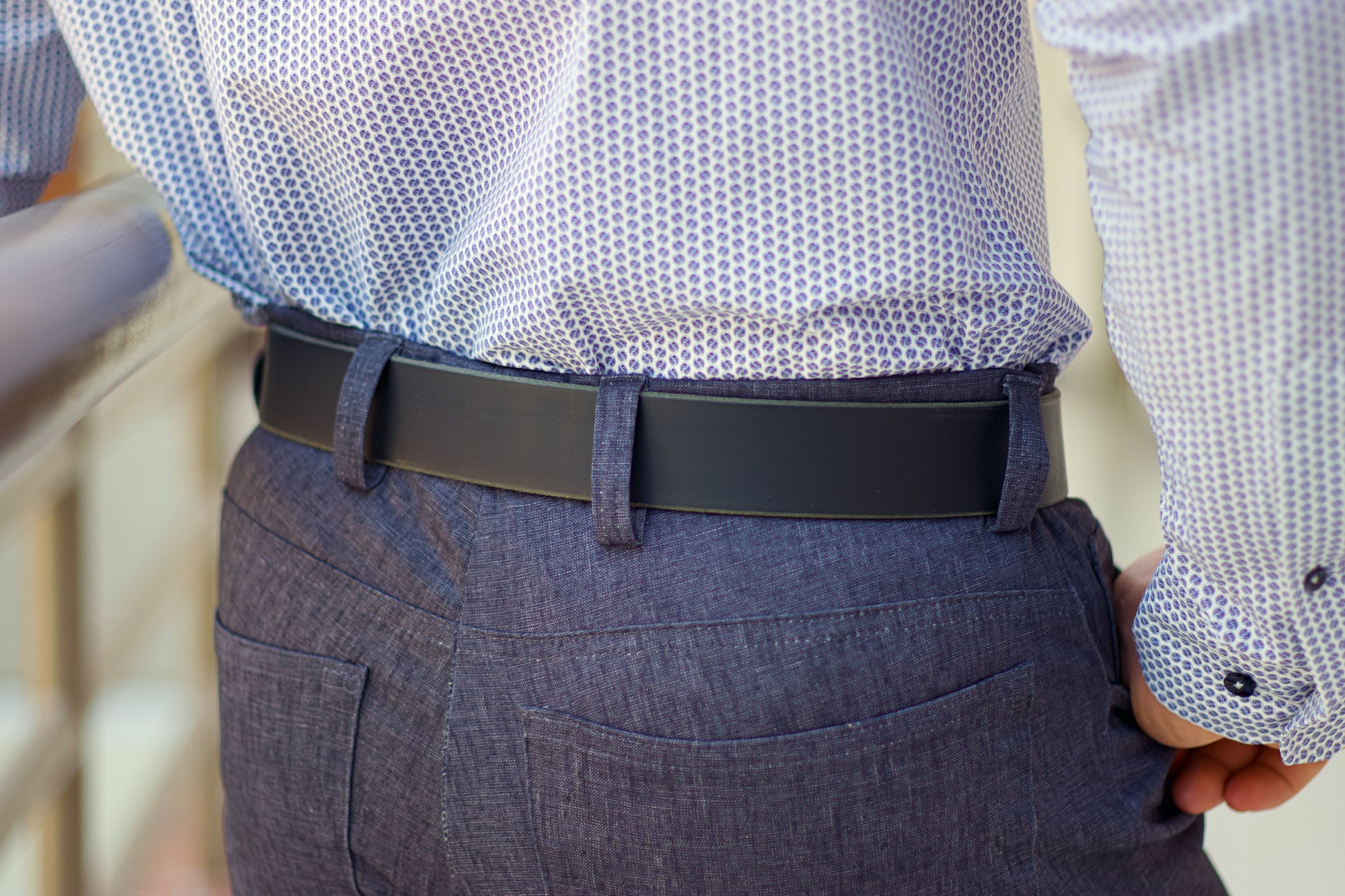 Person wearing a patterned shirt, dark belt, and gray pants.